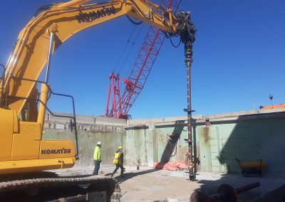 A lead helical pile pole is drilled into the ground under the Solids Building basement.